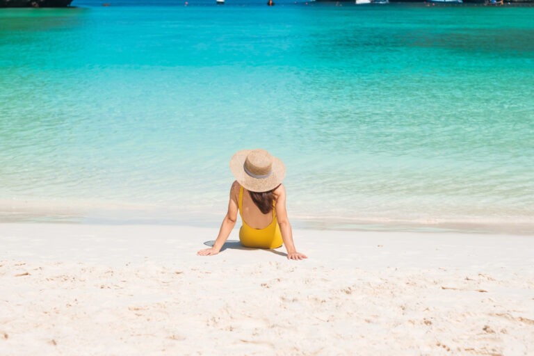 Happy woman in a yellow swimsuit and hat sunbathing at Maya Bay beach, Phi Phi Island, Thailand.